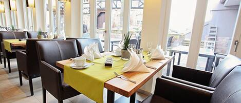 A restaurant with a long table set for two, chairs, and a view of the outside.