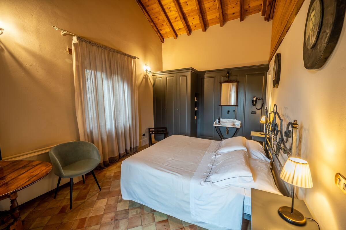 A hotel room with a bed, a chair, a desk, a lamp, and a mirror on the wall.