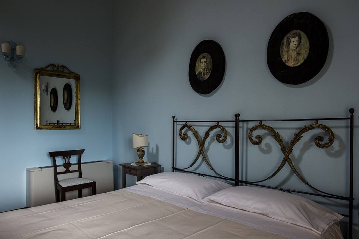 A bedroom with a bed, a chair, a nightstand, a lamp, and two framed pictures on the wall.