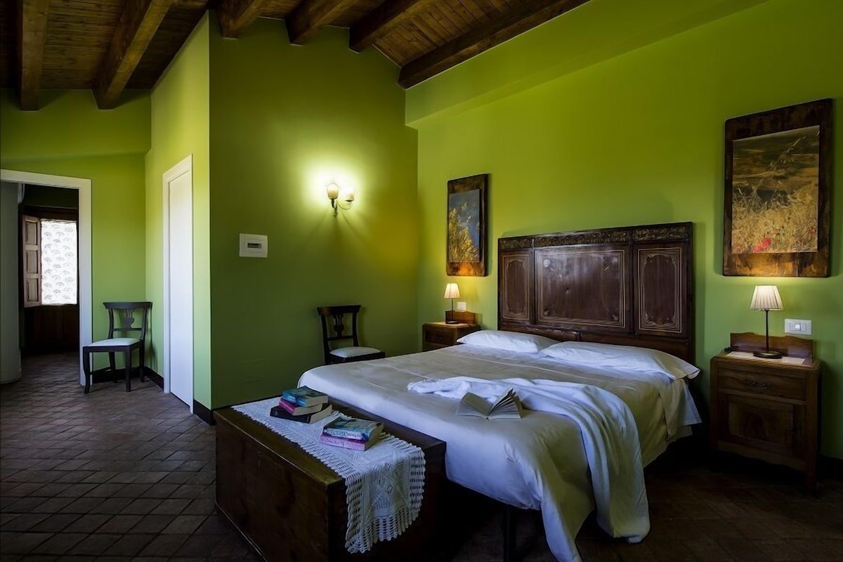 A room with a bed, bedside tables, a chair, a wooden bench, and a wall-mounted light fixture.