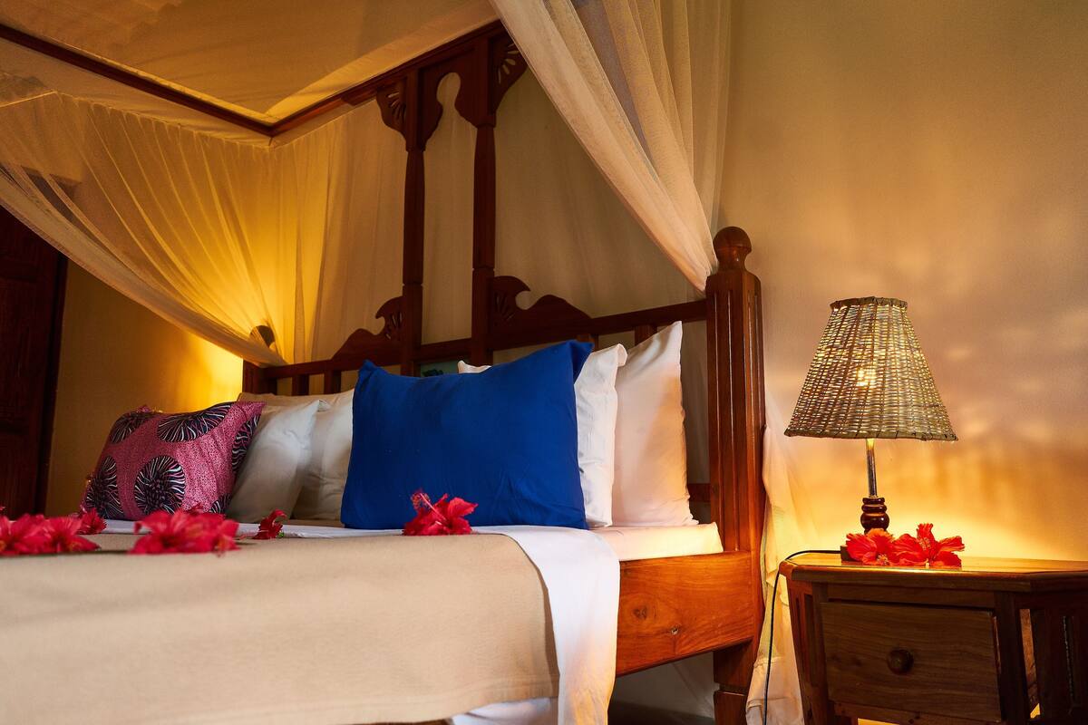 A bed with a canopy, a bedside lamp, and a nightstand with a lamp.