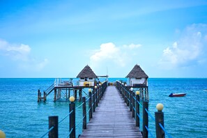 A wooden pier leading to overwater bungalows with thatched roofs, connected by a walkway with railings and spherical posts. - Spice Island Hotel & Resort (Jambiani)