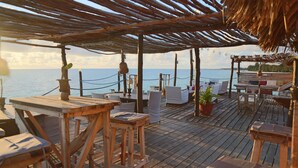 An outdoor wooden deck with white lounge chairs and tables, overlooking the sea.