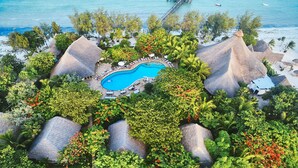 An aerial view of a resort with a central swimming pool surrounded by lush greenery and thatched-roof structures.
