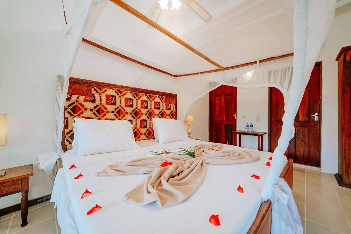 A four-poster bed with a canopy, a patterned headboard, and a bedside table with a lamp.