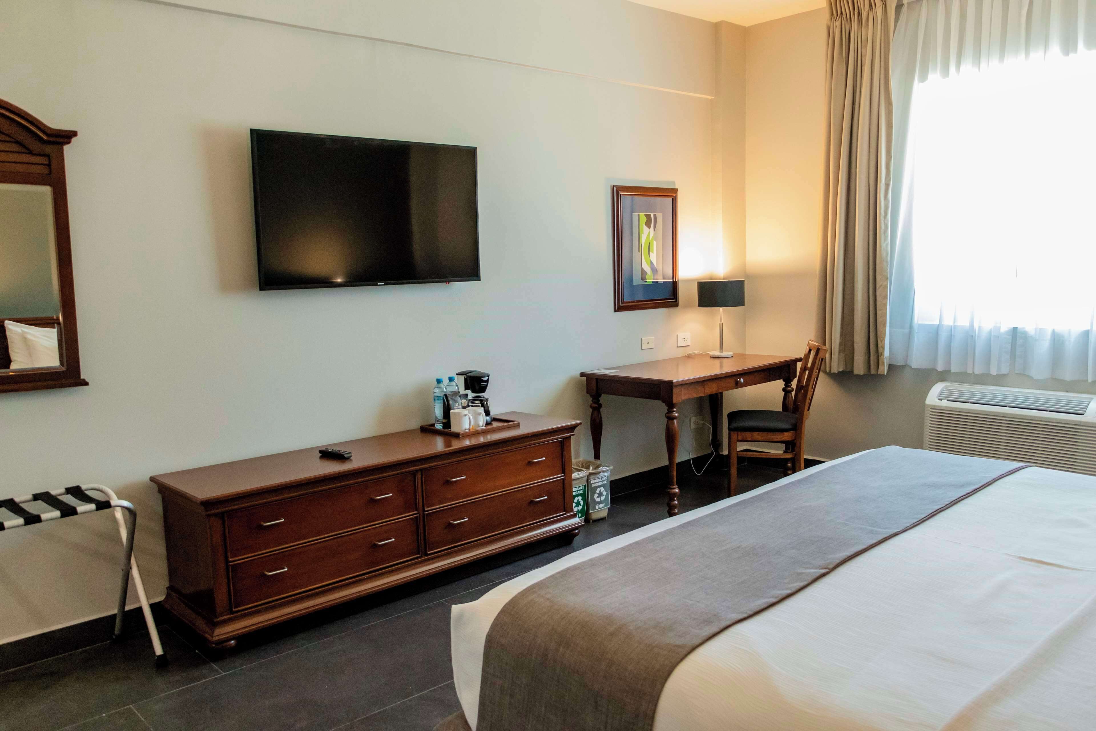 A hotel room with a bed, a desk, a chair, a TV, and a window with curtains.