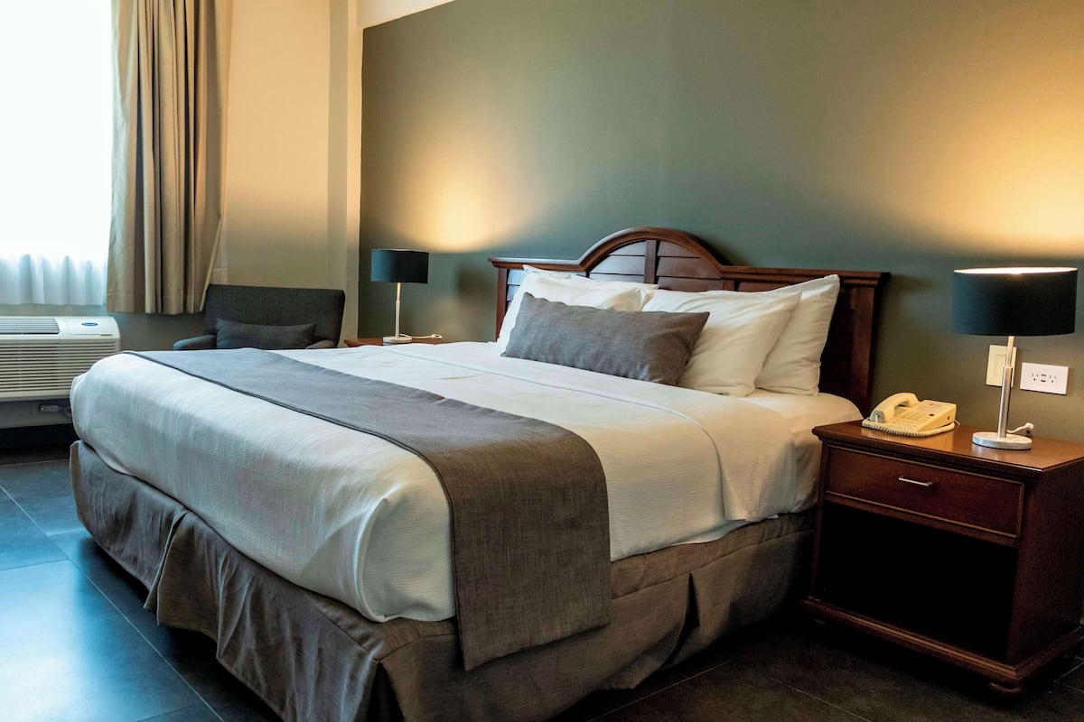 Quarto de hotel com uma cama grande, mesa de cabeceira com abajur, telefone e ar condicionado instalado na parede.