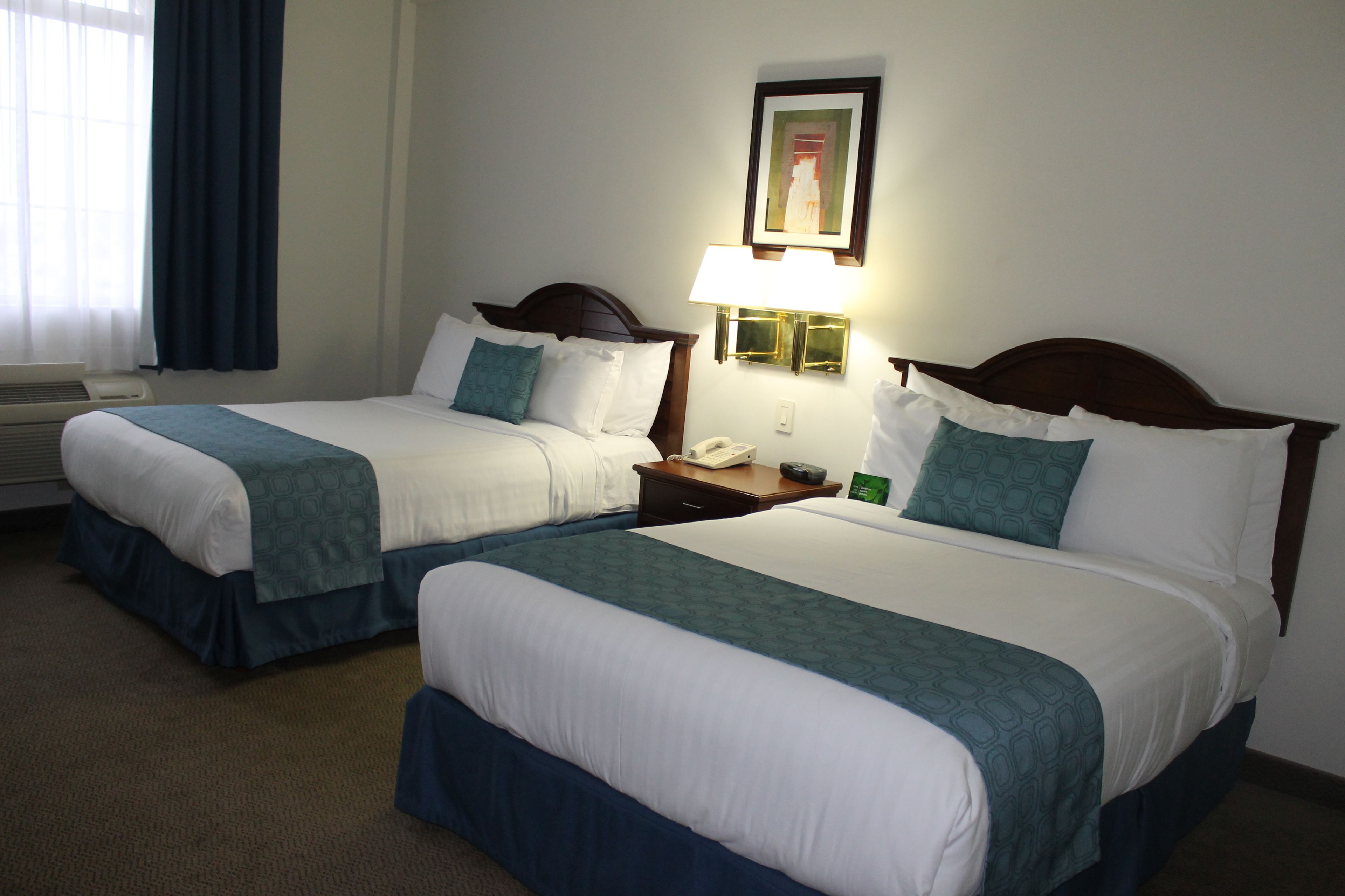 Two twin beds with matching headboards, a bedside table with a lamp, a framed picture on the wall, and a window with curtains.