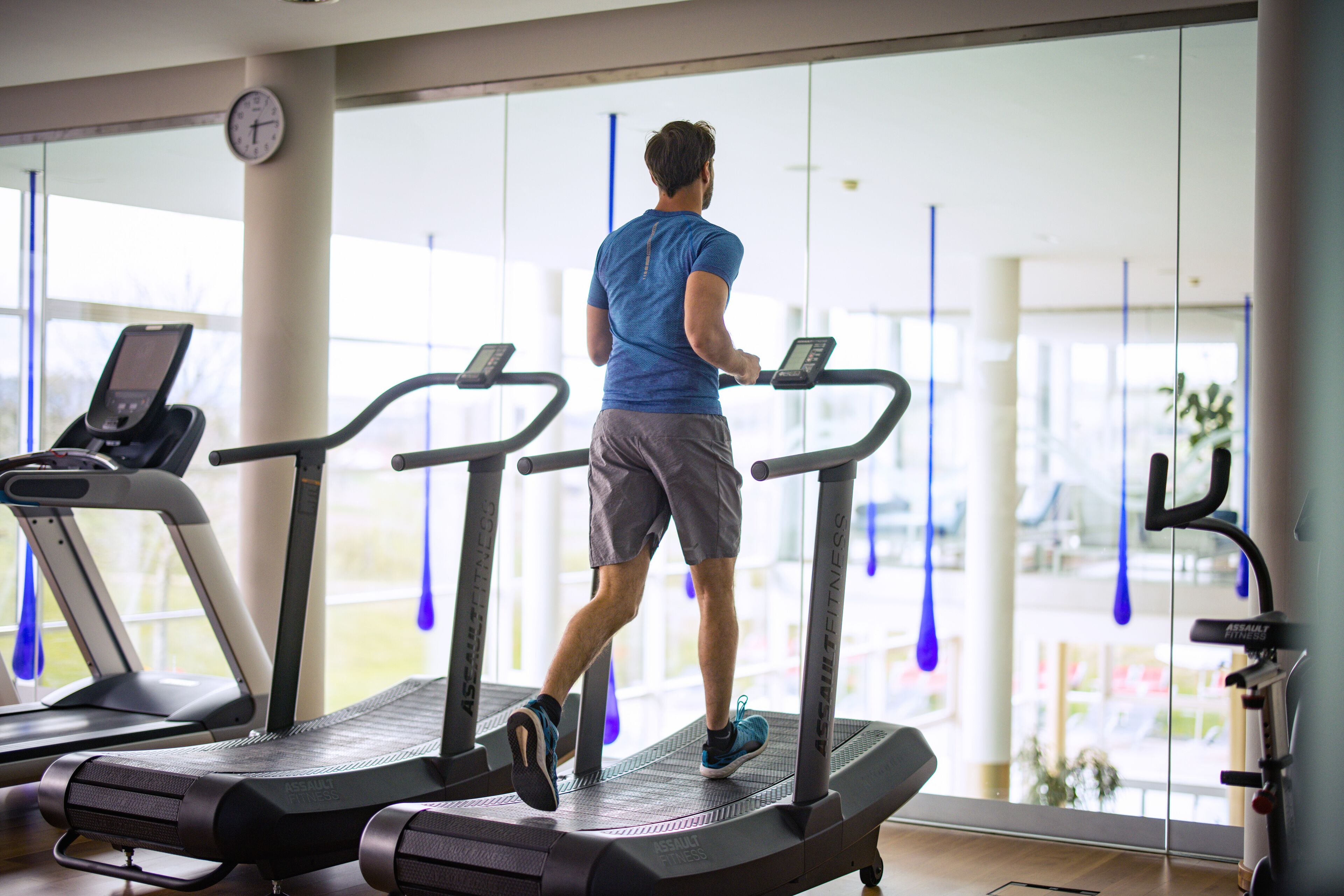A gym with treadmills, a digital clock, and large windows.