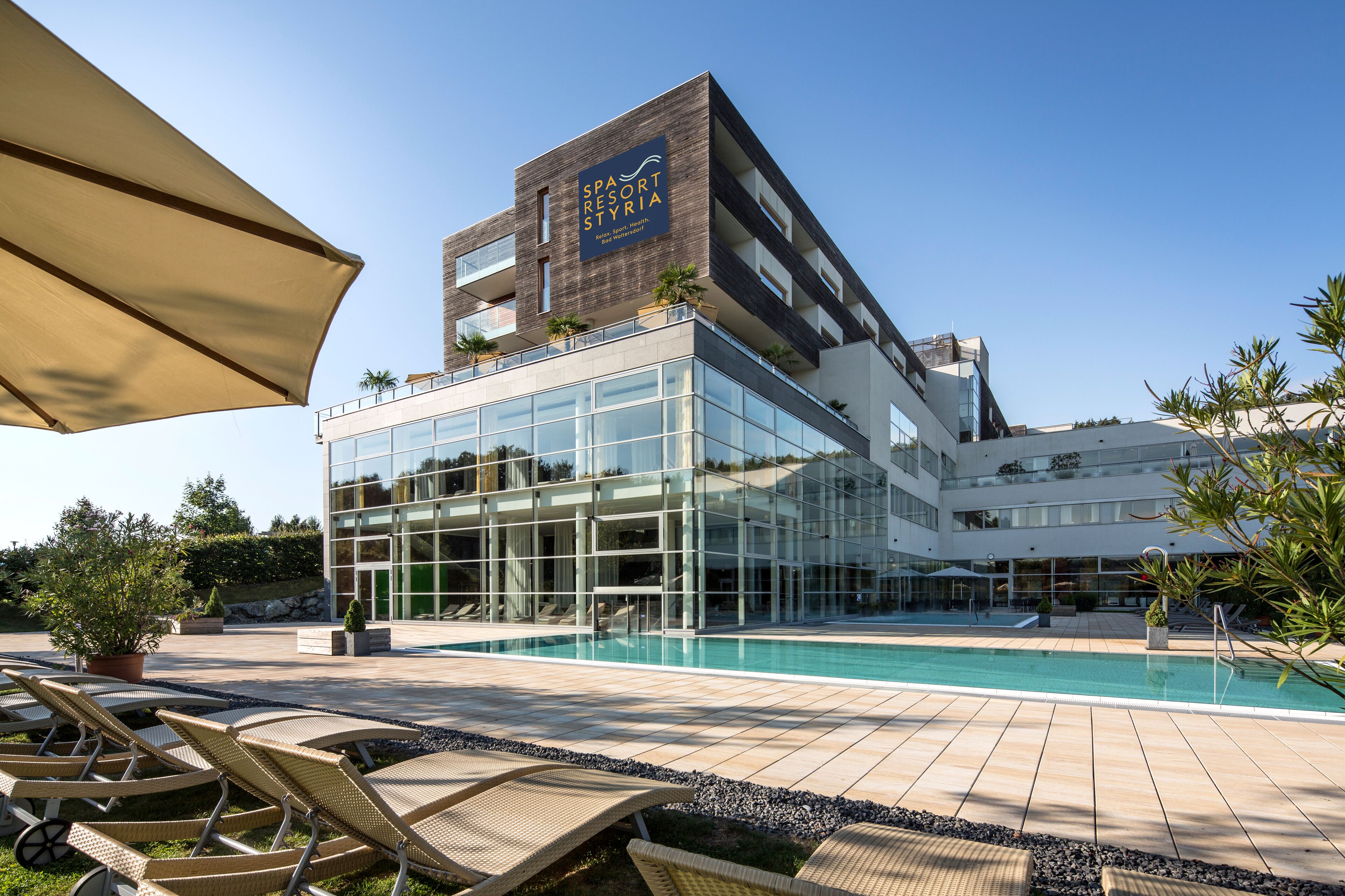 Un hotel moderno con piscina, sillones de descanso y un cielo azul despejado.