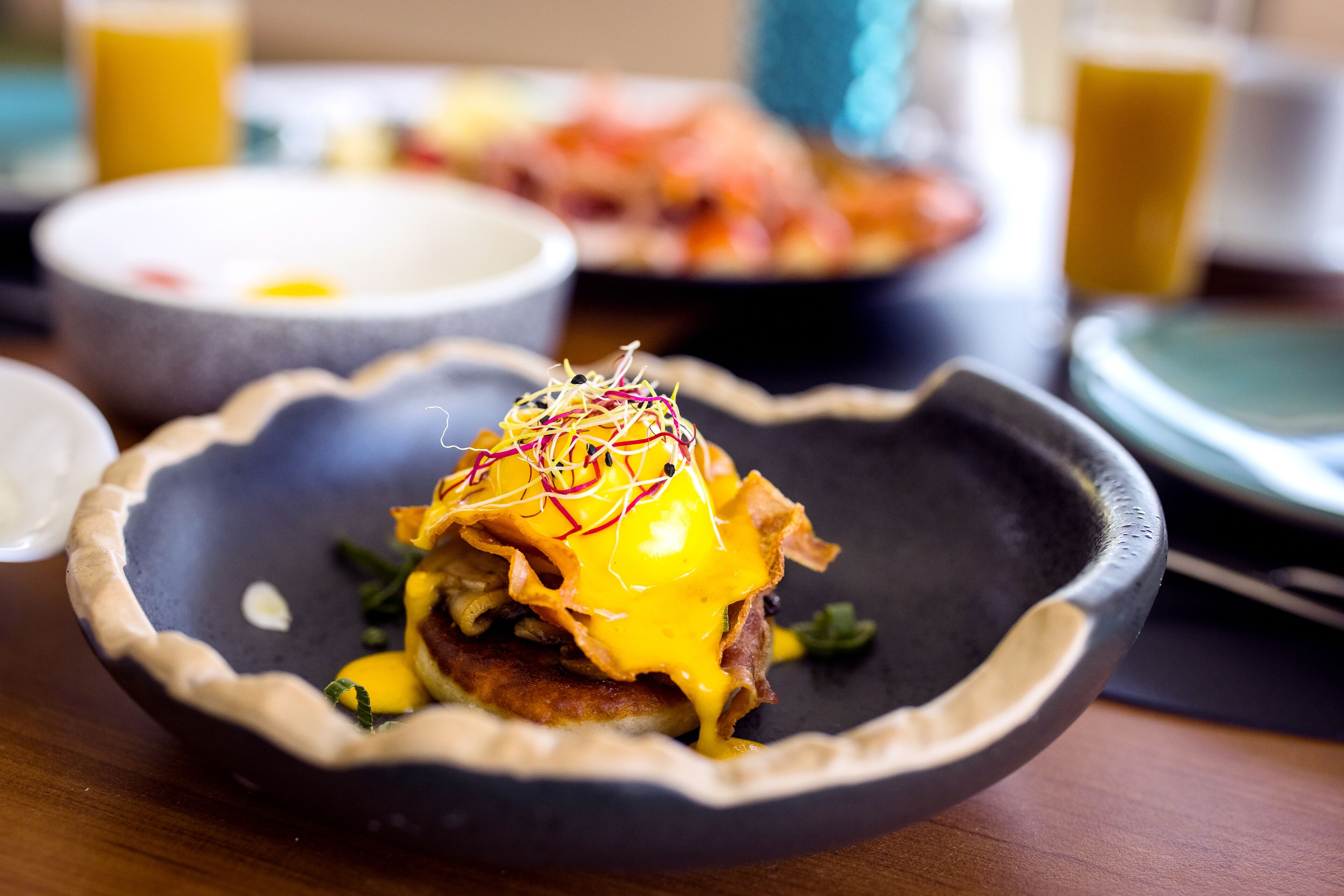 A breakfast dish with a poached egg, hash browns, and a side of greens on a dark plate.