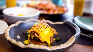 A breakfast dish with a poached egg, hash browns, and a side of greens on a dark plate.
