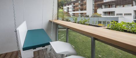 Un balcón con una silla colgante, una mesa de madera y vistas a edificios modernos.