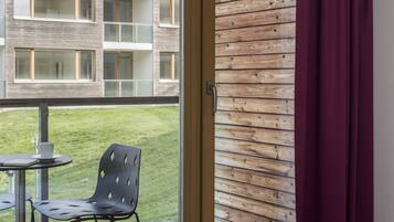 A hotel room with a balcony, a wooden wall, and a view of a building with multiple windows.