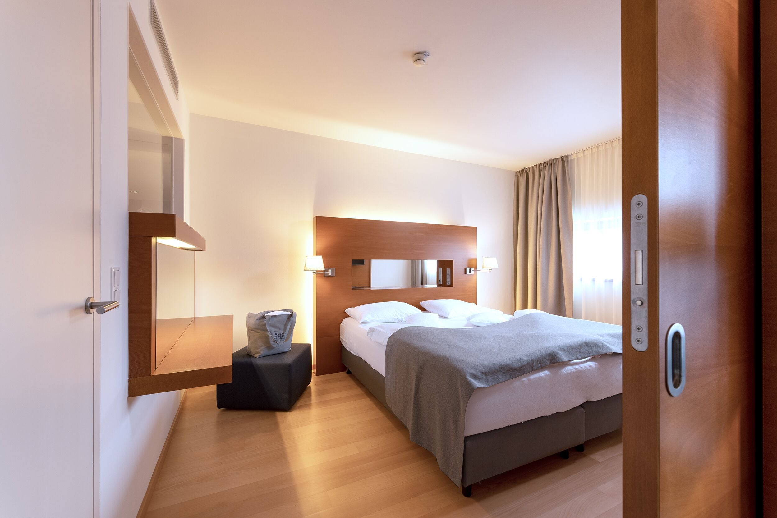 Een hotelkamer met een bed, nachtkastje, lamp en een spiegel aan de muur.