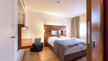Een hotelkamer met een bed, nachtkastje, lamp en een spiegel aan de muur.