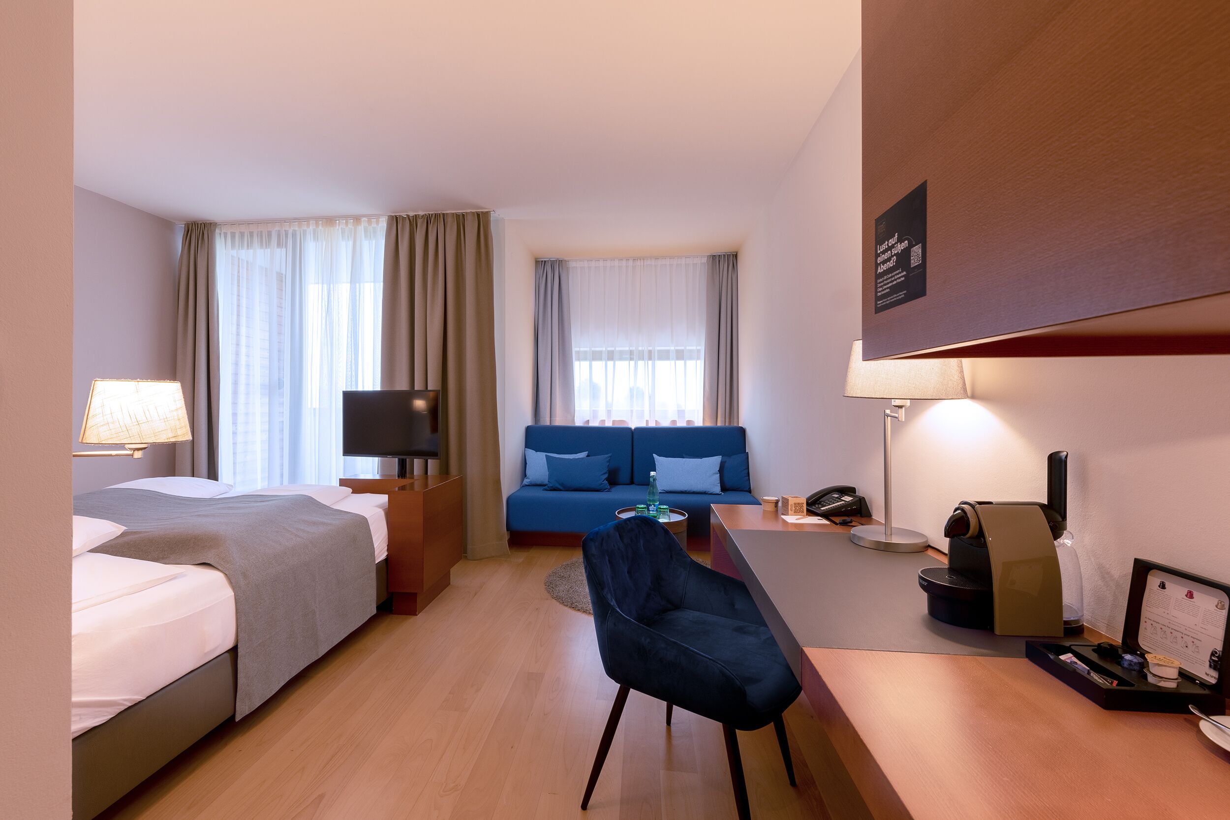 A hotel room with a bed, a desk, a chair, a sofa, and a television.