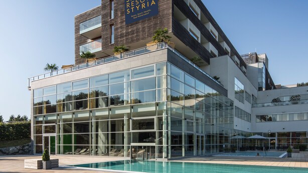 Ein modernes Gebäude mit einem Spa-Resort-Schild, großen Glasfenstern und einem Poolbereich.
