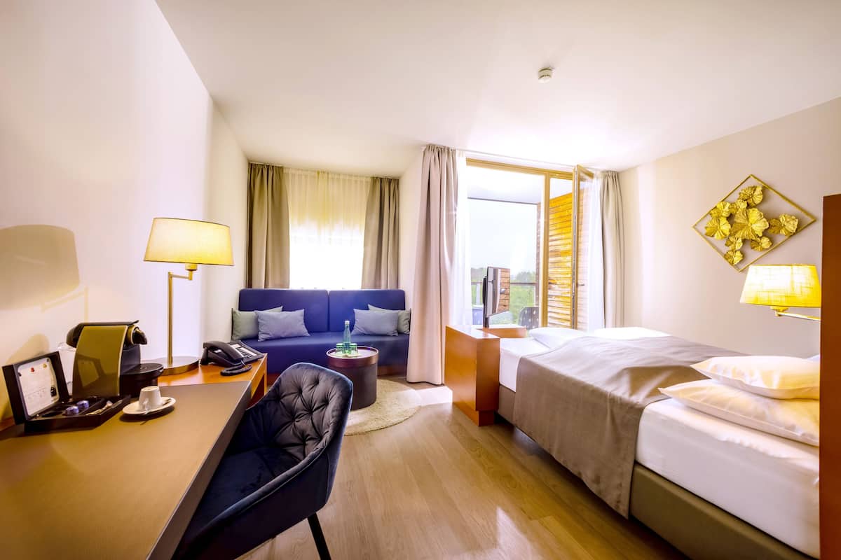 Een hotelkamer met een bed, een slaapbank, een bureau met lamp, een stoel en een raam met gordijnen.