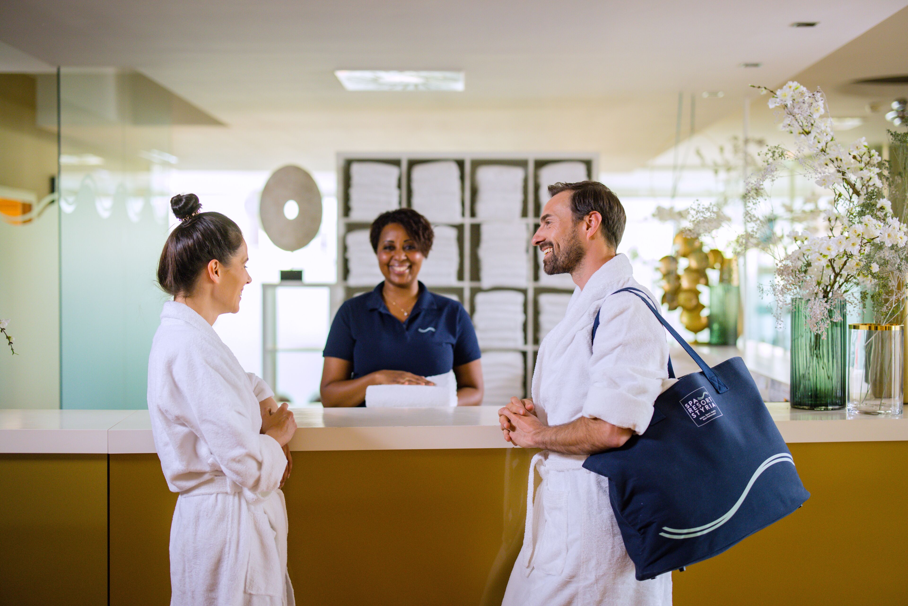 A reception area with a counter, a receptionist, and two guests.