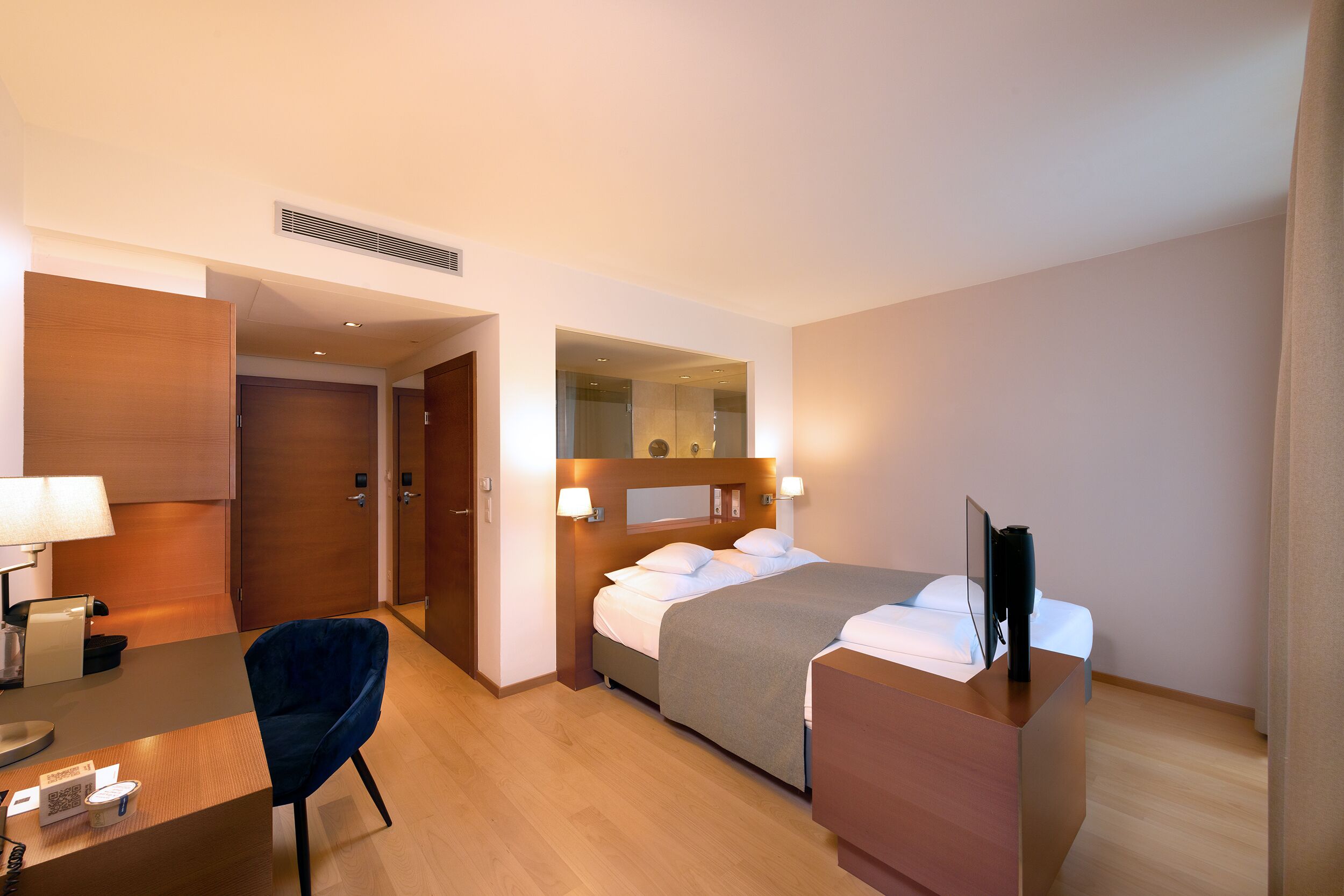 A hotel room with a bed, bedside table, desk, chair, and a mirror.