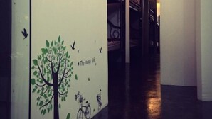 A corridor with a wall mural featuring a tree, birds, and bicycles, and a staircase in the background. - At Phangan Hostel (Ko Pha-ngan)