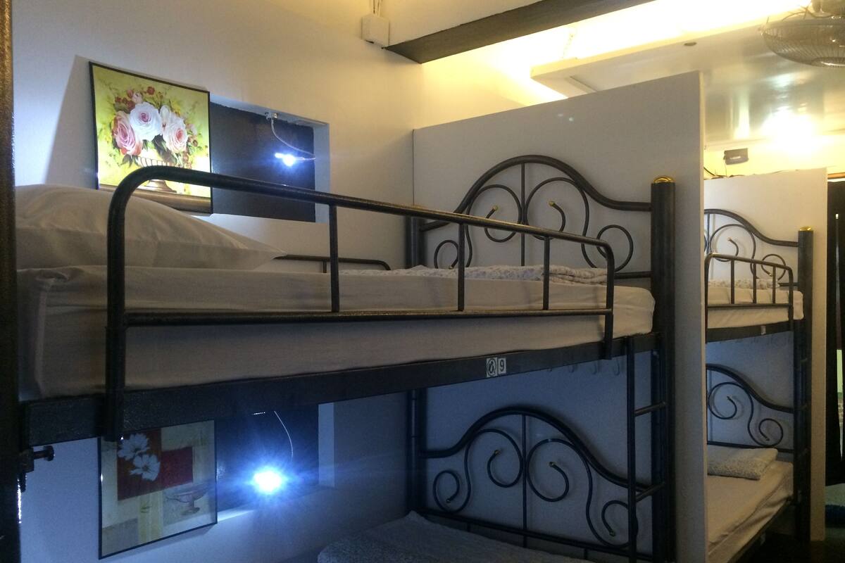 Quarto com beliche, um quadro na parede e iluminação no teto.