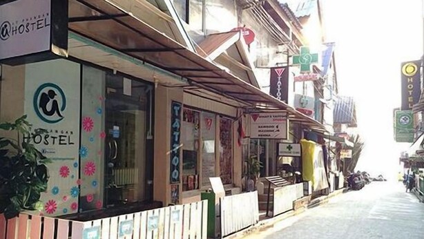 A hostel with a signboard, a window with a floral pattern, and a small outdoor seating area. - At Phangan Hostel (Ko Pha-ngan)