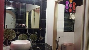 A bathroom with a black tiled wall, a white sink, a mirror, and a toilet. - At Phangan Hostel (Ko Pha-ngan)