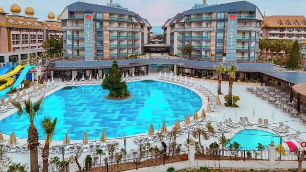 Un hotel con piscina centrale, numerosi balconi e un'area giochi per bambini.