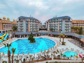 Un hotel con piscina central, varios balcones y una zona de juegos para niños.