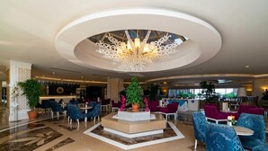 Una hall d'albergo con un'area salotto centrale, un lampadario e una reception.