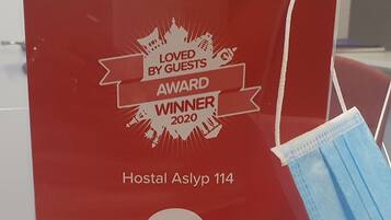 Una placa roja de premio por una calificación de 9/10 de Hoteles.com, sobre una mesa con una mascarilla azul cerca.