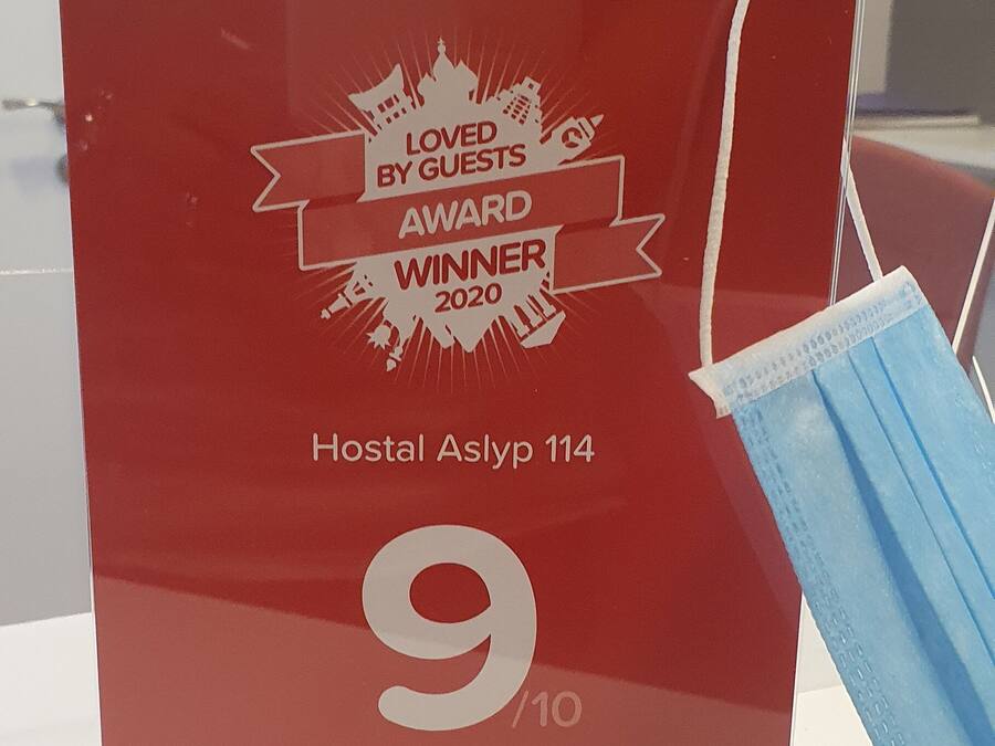 Una placa roja de premio por una calificación de 9/10 de Hoteles.com, sobre una mesa con una mascarilla azul cerca.