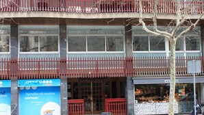 A building with a red balcony, a storefront with a sign, and a tree in front. - Hostal Aslyp 114 (Barcelona)