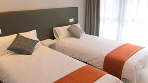 Two single beds with white linens and orange throw blankets, a dark headboard, and a window with sheer curtains. - Hostal Aslyp 114 (Barcelona)