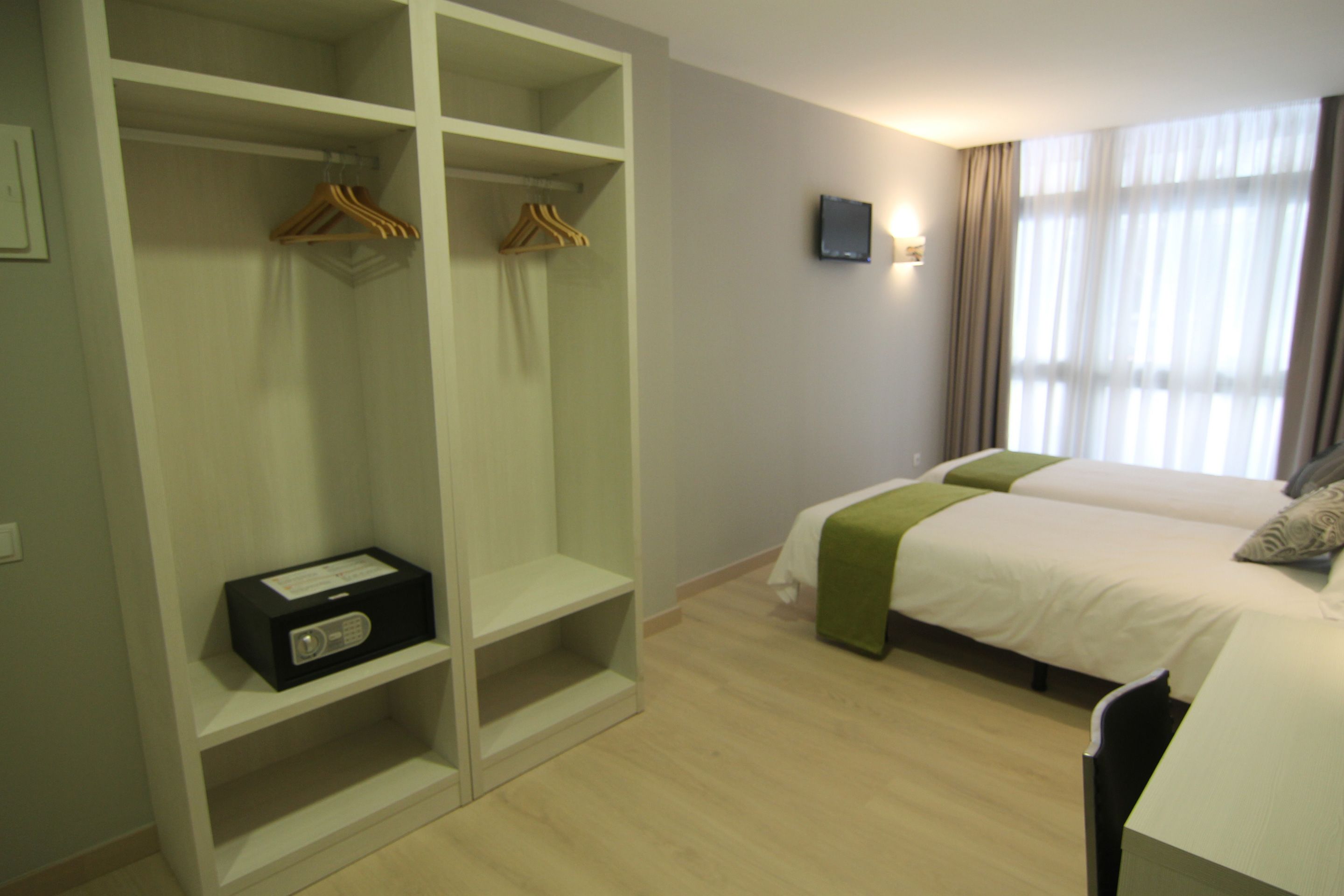 Ein Hotelzimmer mit großzügigem begehbarem Kleiderschrank, einem Bett mit grüner Tagesdecke und einem flachbildfernseher an der Wand.