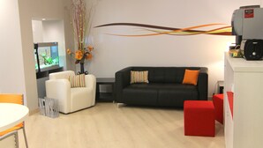 A modern living room with a white sofa, a black sofa with orange cushions, a red ottoman, and a large aquarium. - Hostal Aslyp 114 (Barcelona)