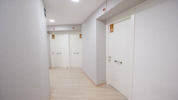 Un pasillo con paredes blancas y piso de madera que conduce a tres puertas cerradas con los números 05, 06 y 07.