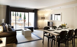 A modern living room with a sofa, a coffee table, and a dining area with a table set for four. - Up Suites Bcn (Barcelona)
