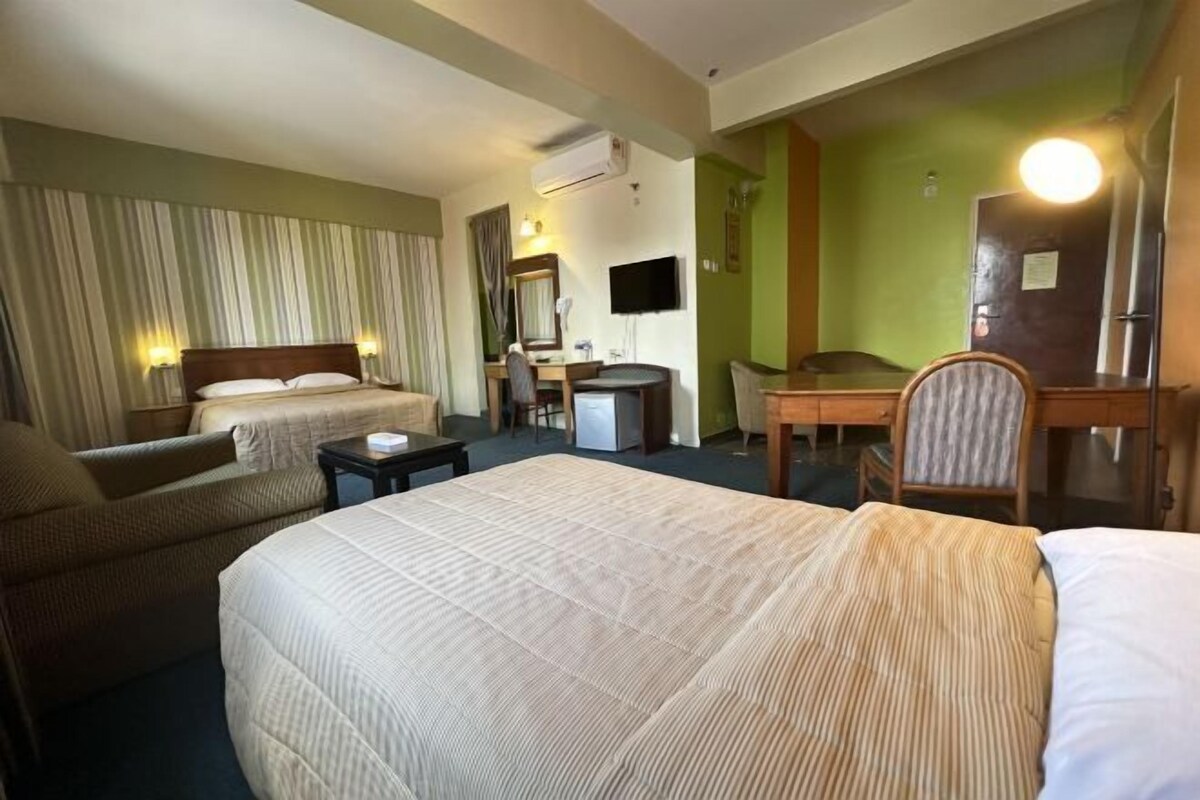 A hotel room with two beds, a desk, a chair, a TV, and a mirror.