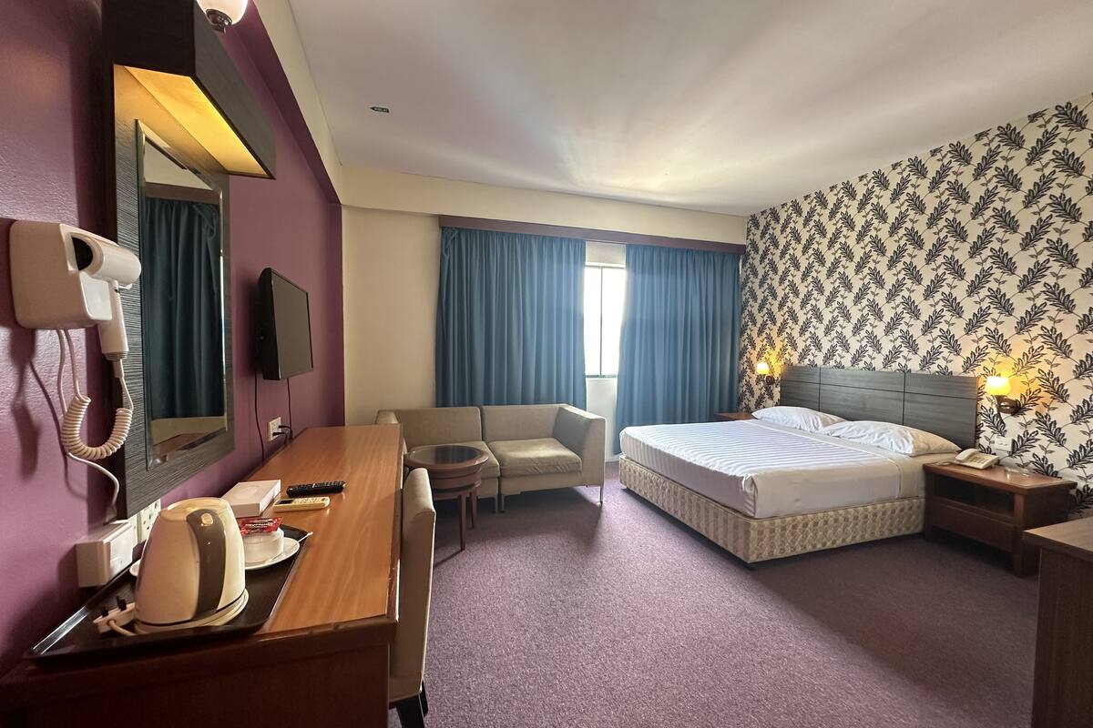 A hotel room with a bed, a desk with a telephone and remote controls, a sofa, a small table, and a mirror.