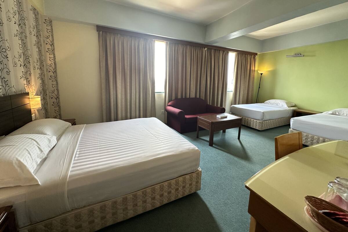 A hotel room with two beds, a chair, a small table, and a lamp.