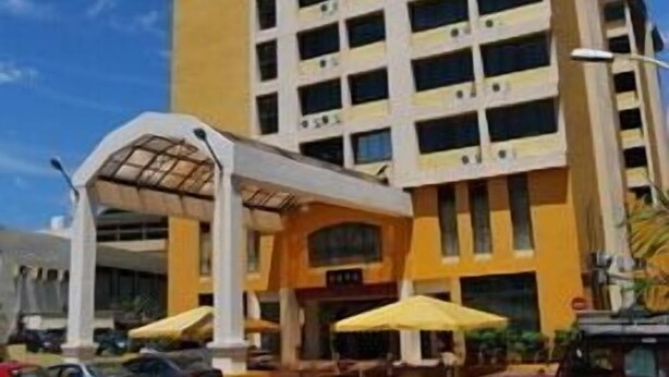 Ein mehrstöckiges Hotel mit gelber Fassade, überdachter Eingangsparte und Außenbereichen mit Sitzgelegenheiten.