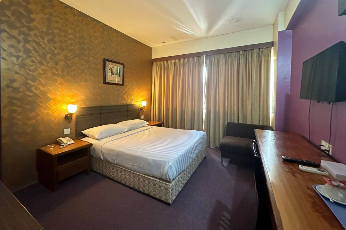 A hotel room with a bed, bedside lamps, a desk with a chair, a telephone, and a television.