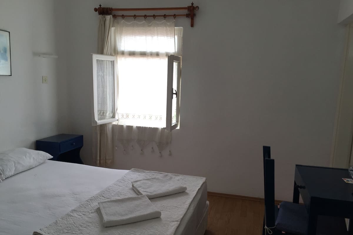 A bedroom with a bed, a desk, and a window with curtains.