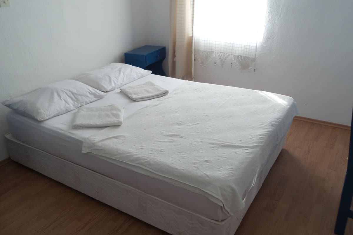 A single bed with white linens, a blue nightstand, and a wooden floor.