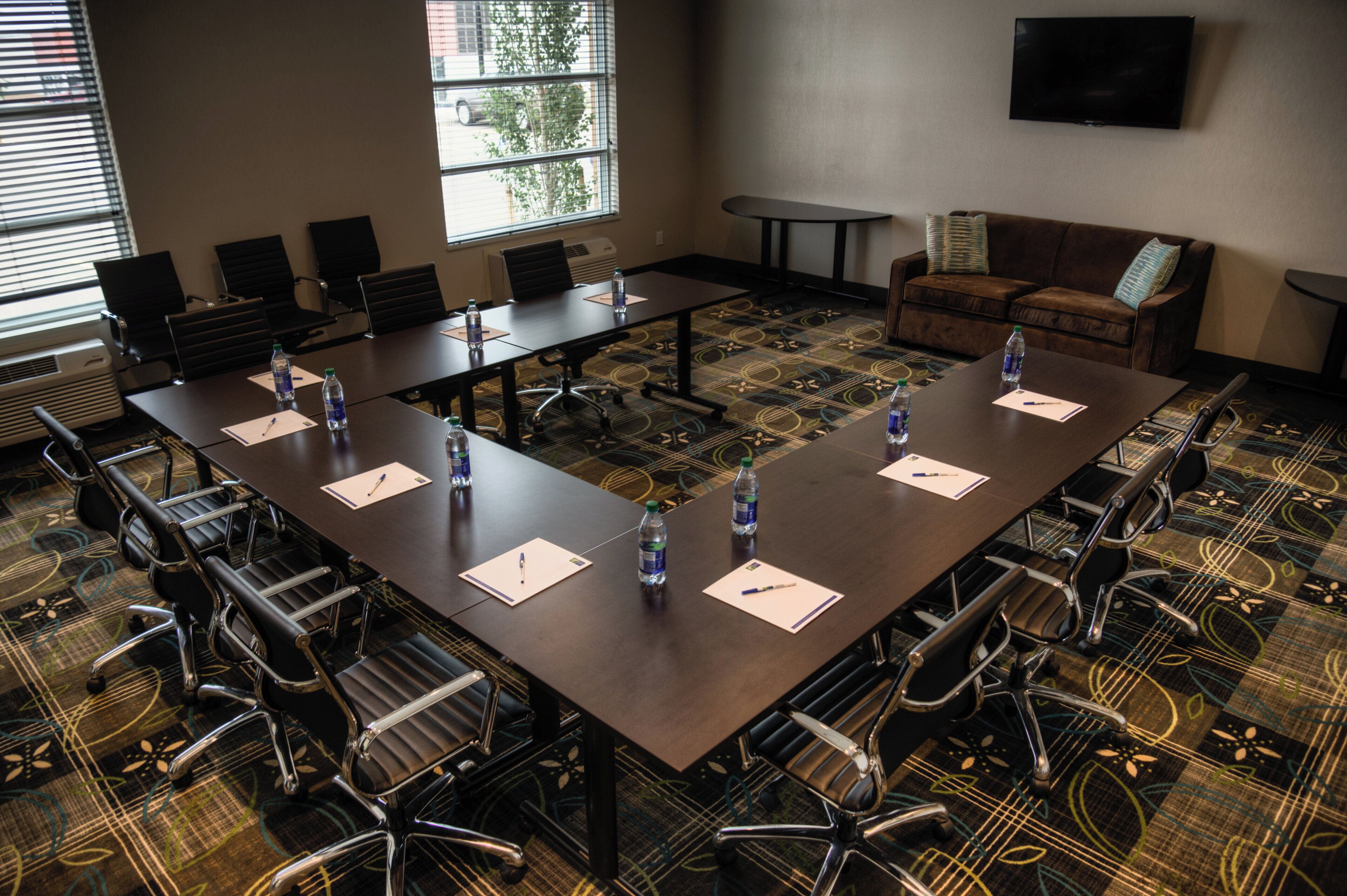 A conference room with a long table, chairs, water bottles, and a television on the wall.