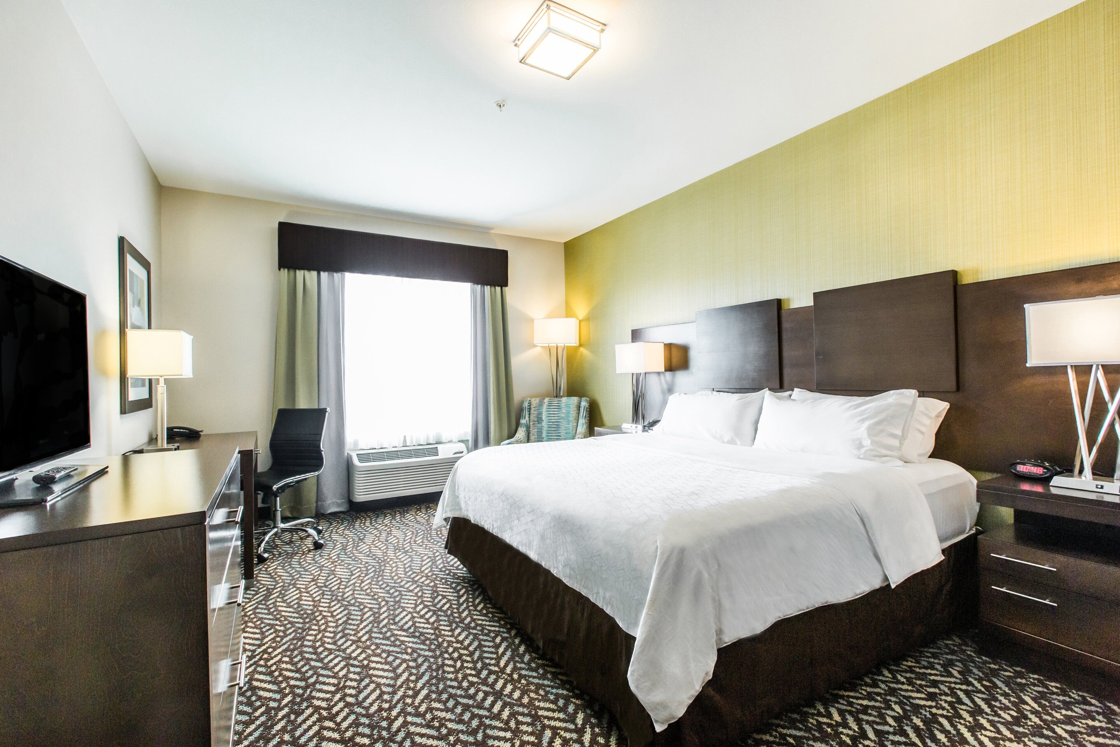 A hotel room with a large bed, a desk with a TV, a chair, and a lamp.