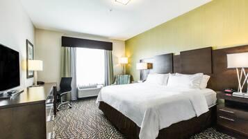 A hotel room with a large bed, a desk with a TV, a chair, and a lamp.